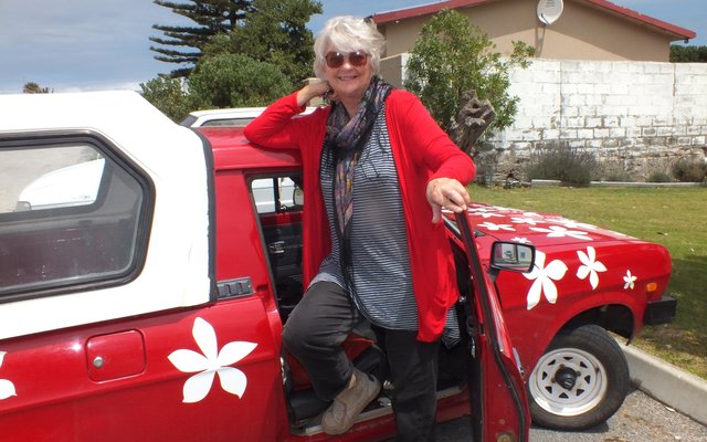  Lyn Greenwood-Smith by haar rooi Nissan bakkie met blomme as versierings waarmee sy en haar suster, Pat Cheetham om Suid-Afrika se buite-grense gery het 